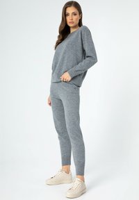 Šedá pletená mikina a odpovídající slim-fit kalhoty, které mají jemnou strukturu a jednoduchý design, doplněné o světlé tenisky.