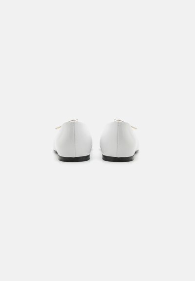 White leather shoes with a smooth texture, minimalistic design, and contrasting black soles, featuring laces on the back.