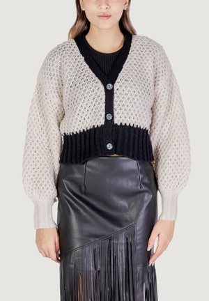 Cardigan all'uncinetto in beige e nero con grandi bottoni, orlo a coste e maniche a palloncino abbinato a una gonna di pelle nera con frange.