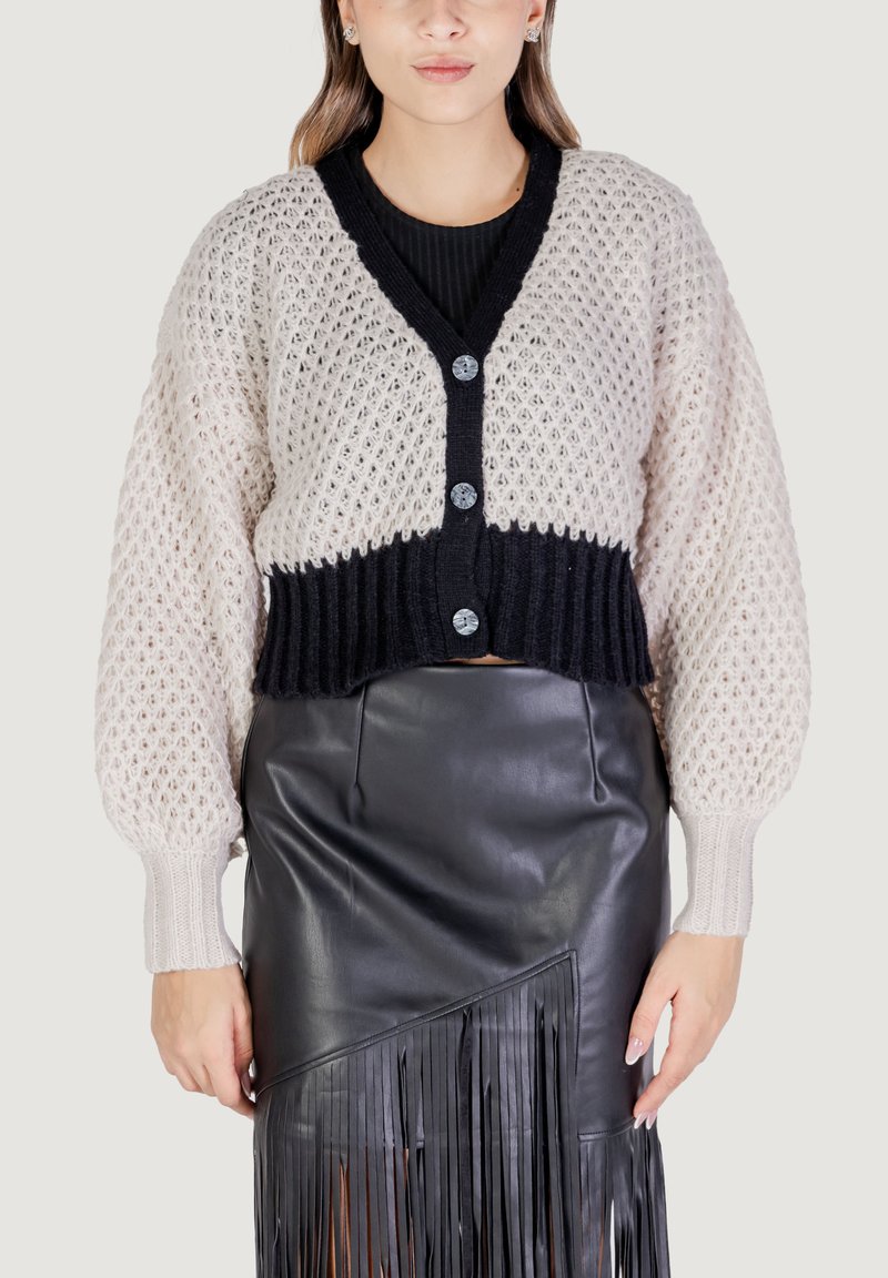 Cardigan all'uncinetto in beige e nero con grandi bottoni, orlo a coste e maniche a palloncino abbinato a una gonna di pelle nera con frange.