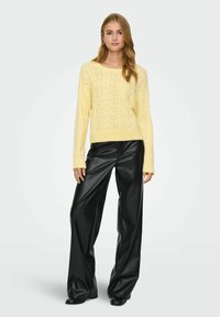 Pull jaune tricoté avec motif texturé et encolure large, associé à un pantalon large en similicuir noir. Matière douce, coupe décontractée.