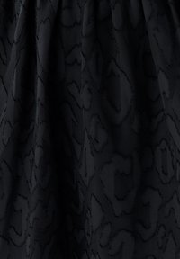 Juoda medžiaga su subtiliu iškilusiu leopardžio rašto paviršiumi ir minkštais klostėmis.