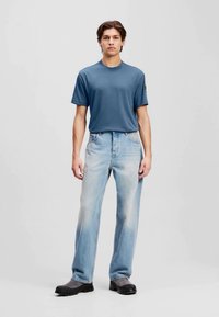 T-shirt azul com decote redondo, em tecido suave, combinado com jeans de perna reta azul claro, com lavagem desbotada, e botins pretos até ao tornozelo. Design simples, sem padrões.