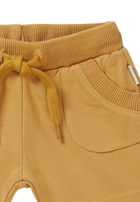 Pantalons de survêtement couleur moutarde avec une taille côtelée, un cordon de serrage et des poches latérales. Texture douce avec une finition lisse.