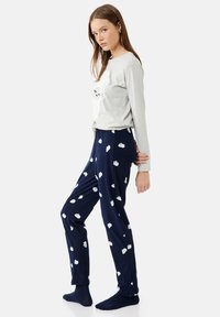 Grå langærmet pyjamatrøje med et sky-tryk, parret med marineblå bukser med spredte hvide sky-mønstre. Blødt bomuldsstof.