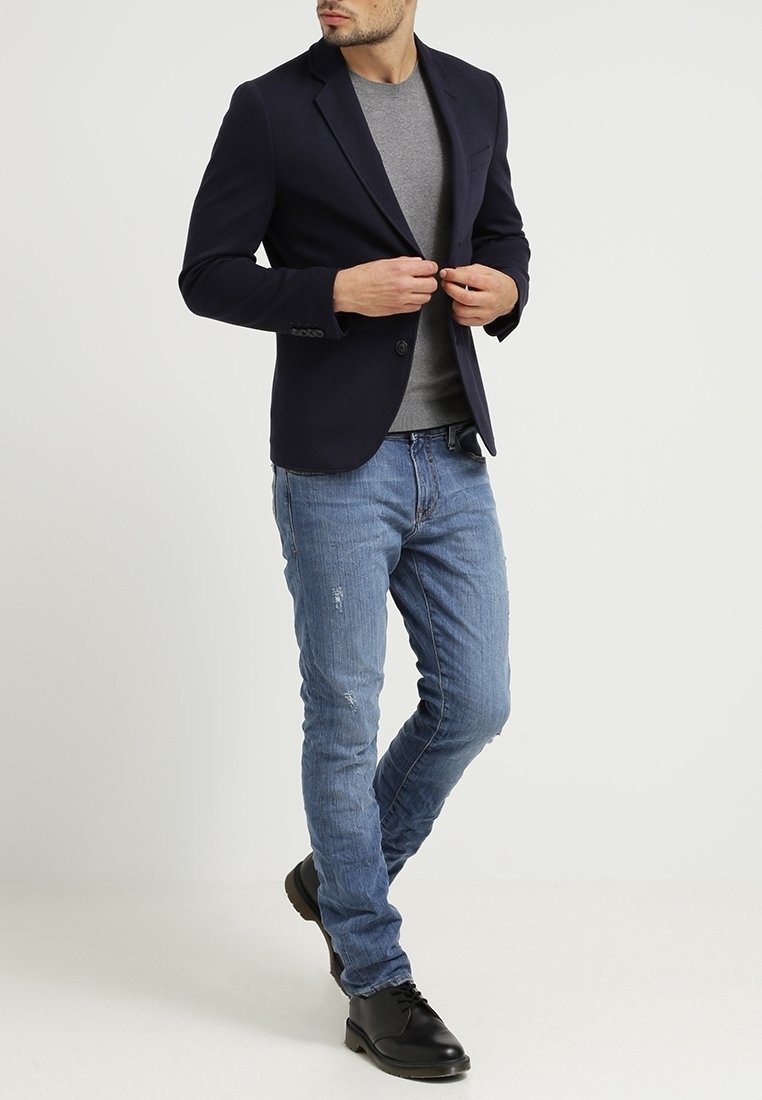 Navy blazer over a grey shirt, paired with light blue distressed jeans and black shoes. Features structured fit and classic design elements.
