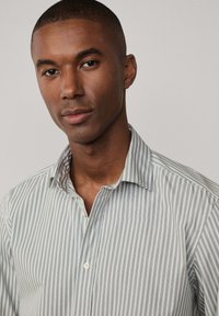 Camicia a righe con colletto button-up, caratterizzata da sottili righe verticali grigie e bianche, realizzata in un tessuto morbido con una vestibilità comoda.