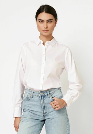 Weißes Hemd mit Kragen aus glattem Baumwollstoff, mit durchgehender Knopfleiste und langen Ärmeln, getragen zu hellblauen, hoch geschnittenen Jeans.