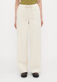 Cream-colored, wide-leg pants with a drawstring waist, featuring front pockets and a smooth, soft texture.