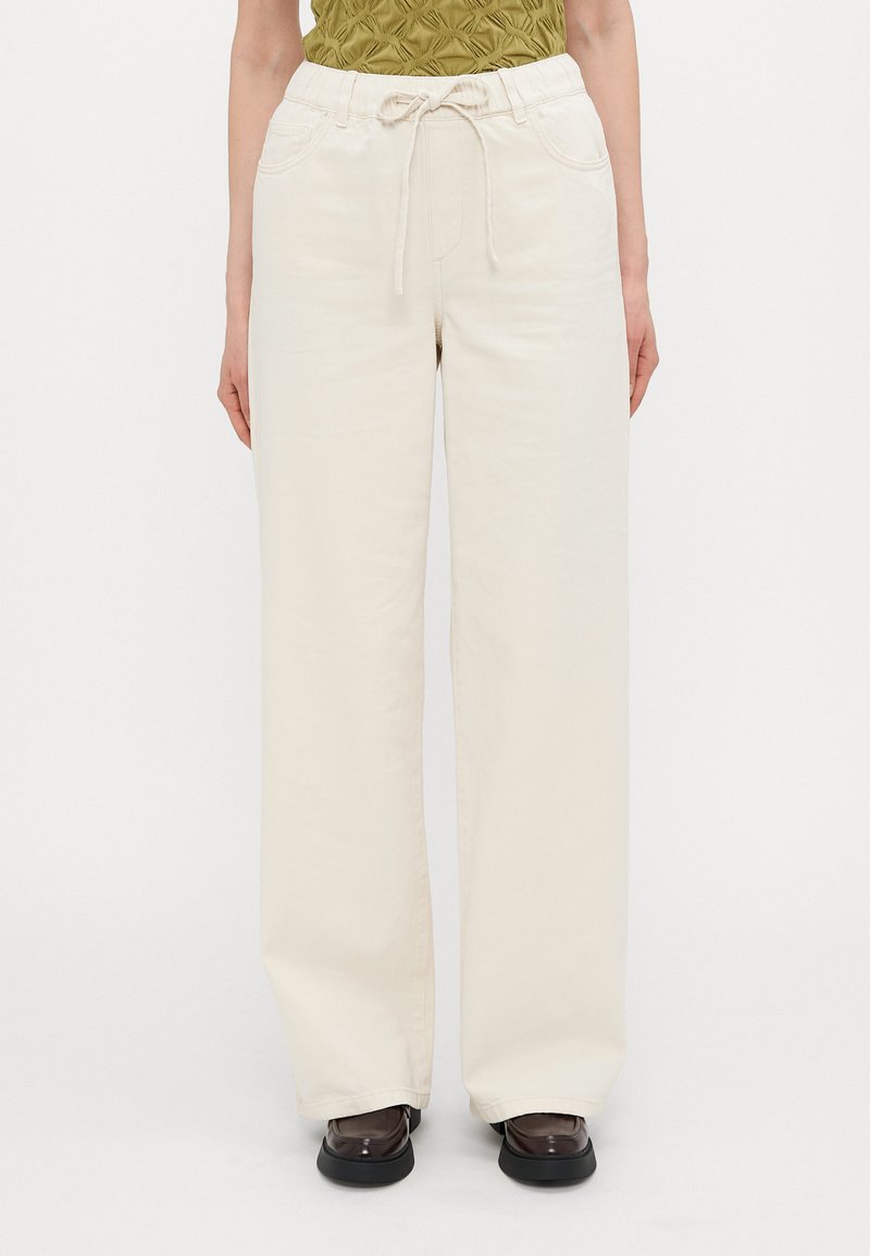 Cream-colored, wide-leg pants with a drawstring waist, featuring front pockets and a smooth, soft texture.