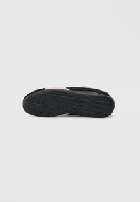 Črne športne čevlje z teksturirano črno gumijasto podplatom, ki imajo rožnati akcentni del blizu pete in gladko zgornjo površino.