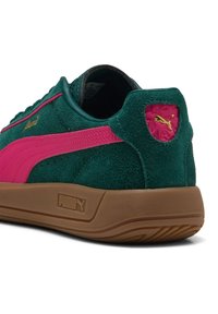 Grüne Wildledersneaker mit rosa Akzenten und goldener Markenkennzeichnung. Verfügt über eine strukturierte Ferse mit Logo, Gummisohle und gestickten Details.