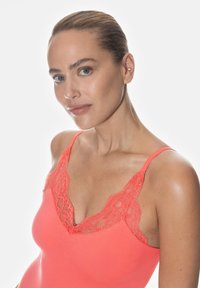 Koronkowy top na ramiączkach w kolorze koralowym z cienkimi regulowanymi ramiączkami i miękką teksturą. Dekolt ma kształt litery V, podkreślający koronkowe wykończenie.