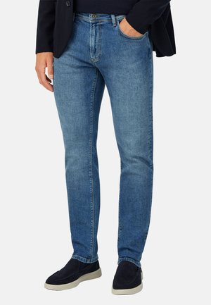 Jeans in denim blu con una vestibilità slim, caratterizzati da leggeri sbiadimenti, un classico design a cinque tasche e una chiusura con zip. Indossati con scarpe scure senza lacci.