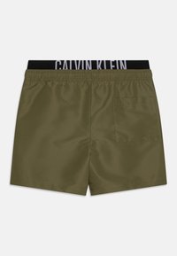 Olive spalvos maudymosi šortai su juodu elastingu juosmeniu, ant kurio yra baltas "CALVIN KLEIN" prekės ženklas. Į komplektą įeina užpakalinis kišenė su atvartu.