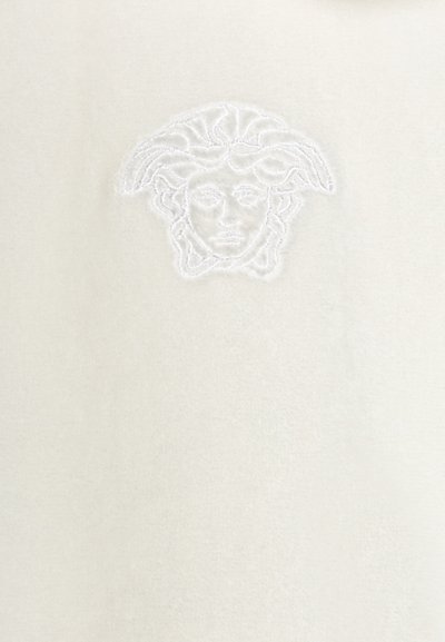 Tissu blanc avec une texture douce, comportant un logo Méduse brodé en fil blanc au centre.