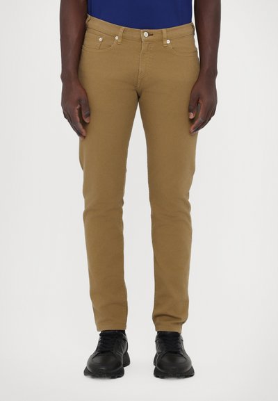 Khaki slim-fit kalhoty s hladkým povrchem, pěti kapsami a poutky na opasek. V kombinaci s černými sportovními botami.