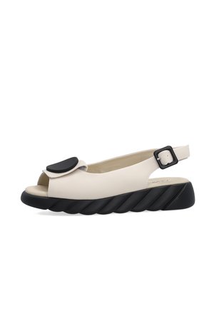 Beżowa sandałka typu slingback z czarną fakturowaną podeszwą, odkrytymi palcami, regulowanym paskiem z klamrą oraz ozdobnym czarnym akcentem z przodu.