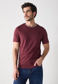 Camiseta de manga corta burdeos con un cuello redondo acanalado en blanco y negro, que presenta un sutil detalle de logo en el pecho. Tejido de mezcla de algodón.