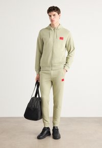 Light green zip-up hoodie and matching joggers, both with red logo accents. Black sneakers and a black bag complete the outfit.