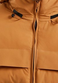 Brązowa ocieplana kurtka z wysokim kołnierzem, zamkiem na suwak i czarnymi akcentami. Dwie przednie kieszenie z patkami. Gładka, wodoodporna tkanina.