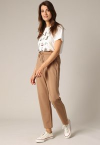 T-shirt graphique blanc avec des motifs colorés, pantalon beige avec cordon de serrage et baskets blanches ; tissu lisse et coupe décontractée, conçu pour le confort.