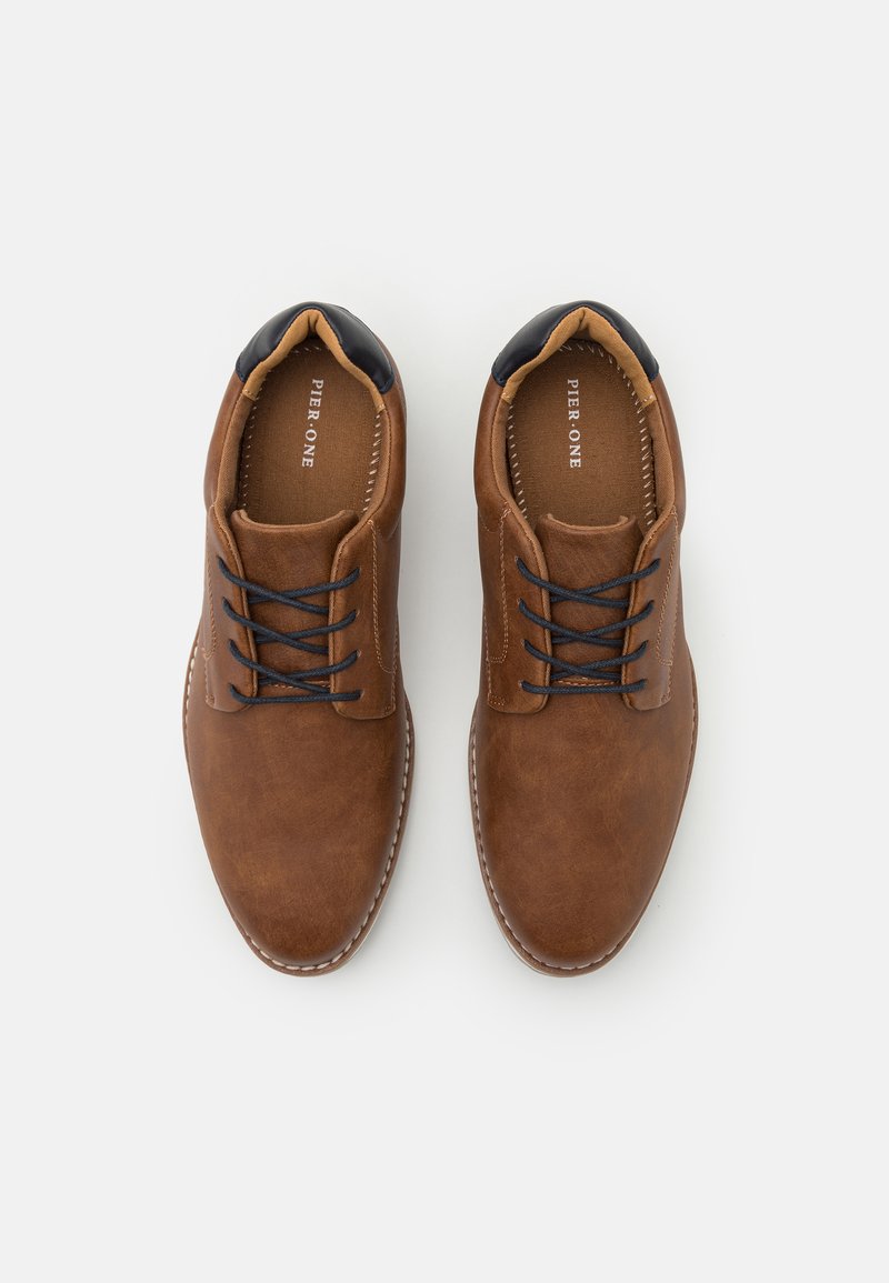 Zapatos de cuero marrón con una textura suave, diseño con cordones y acentos en azul marino en el cuello. Detalles de costura alrededor de la suela.