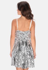 Stříbrné flitrové šaty s tenkými ramínky, přiléhavým tělem a rozšířenou sukní. Zadní část má výstřih ve tvaru lžíce a průhlednost.