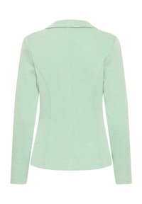 Blazer femme vert clair sur mesure avec manches longues, détails de coutures au dos et col à revers.