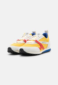 Men's sneakers with a yellow mesh upper, white suede accents, red and blue detailing, and a black rubber sole. Laces and logo on tongue.