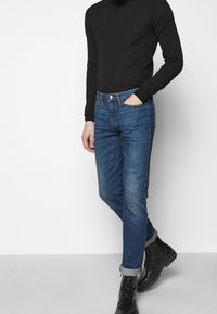 Slim-fit jeans i medelblå denim, med femficksdesign, sömda uppvikta benslut och metallknappstängning, kombinerat med en svart långärmad topp.