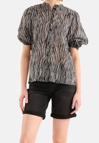 Černobílá zebra pruhovaná průhledná blůza se stojáčkem a balónovými rukávy, zapínání na knoflíky vpředu, spárovaná s ohrnutými černými šortkami.
