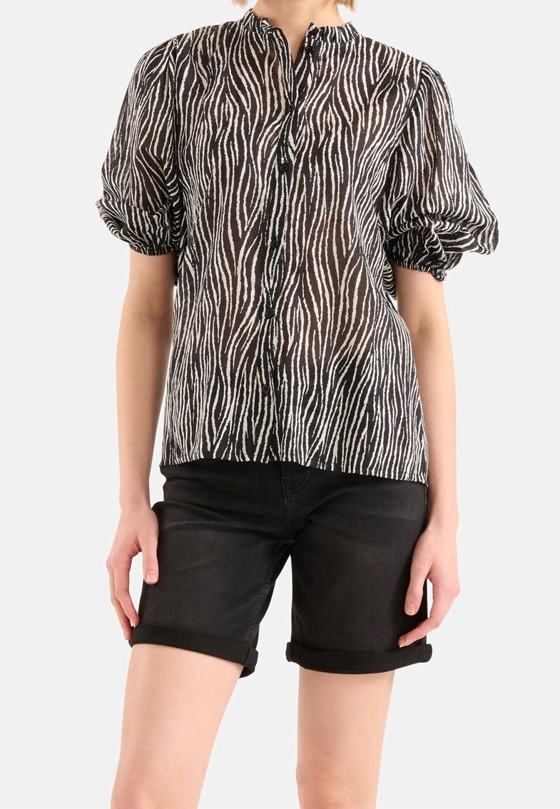 Černobílá zebra pruhovaná průhledná blůza se stojáčkem a balónovými rukávy, zapínání na knoflíky vpředu, spárovaná s ohrnutými černými šortkami.
