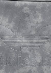 Wytłoczone logo koniczyny Adidas na teksturowanej szarej powierzchni z napisem „adidas” poniżej emblematu.