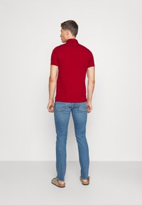 Rød polo skjorte, kort ermer, figursydd design. Brukes med blå jeans. Sett fra bak, viser nakke og skulder. Myk tekstur.