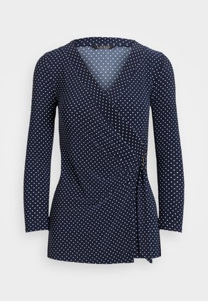 Marineblauwe wikkelblouse met lange mouwen, witte polkadots en een zijstrikdetail.