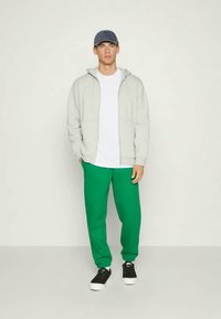 Gray zip-up hoodie, white t-shirt, and green sweatpants. Black sneakers with white soles. Blue cap. Simple, casual athletic style.