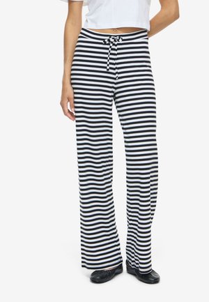 Mujer con pantalones anchos de rayas horizontales en blanco y negro, con cintura de cordón y zapatos negros sin cordones.