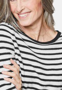 Schwarz-weiß gestreifter Pullover, gestrickte Textur, runder Ausschnitt, Modell mit sichtbarem Schulter, Hand auf dem Arm ruhend, heller Hintergrund.