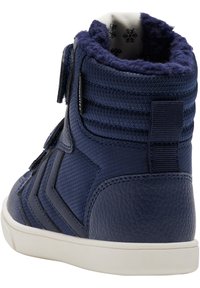 Marinblå hög sneakers med texturerad tyg, vadderad krage och kardborreband. Vit gummisula med spårmönster för grepp.