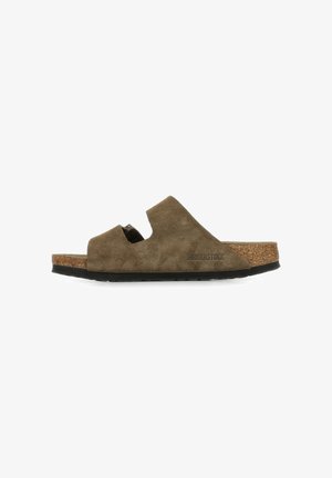 Sandalia tipo slip-on de ante marrón con plantilla de corcho, presenta un diseño con recortes y suela de goma negra texturizada. Logo de la marca visible en el lateral.