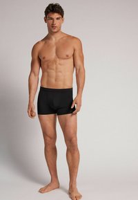 Černé boxerky v těsném střihu vyrobené z měkké tkaniny. Mají jednobarevný design, hladký pas a otvorem vpředu.