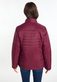 Mørkerød pufferjakke med en quilted tekstur og opretstående krave. Har en glat overflade og en tætsiddende silhuet, parret med blå jeans.