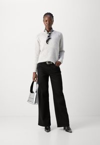 Light gray sweater with ribbed texture, paired with black wide-leg jeans. Accessorized with a black and white scarf and a silver handbag.
