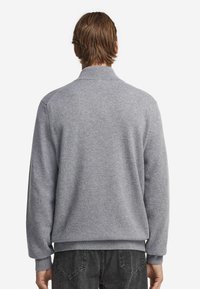 Grå stickad tröja med hög krage, ribbade ärmslut och fångande textur; bakvy visar en avslappnad passform och sömlösa axlar.