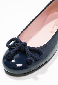 Ballerine bleu marine brillante avec un gros nœud torsadé sur le bout et une doublure intérieure rose clair.