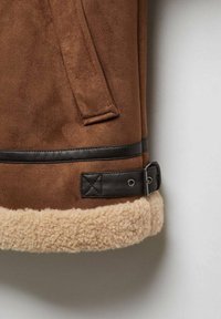 Bruine suède jas met een zwarte leren riemdetail en beige schapenwolafwerking aan de onderrand.