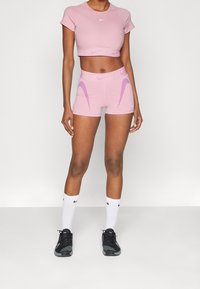 Rosa idrotts crop top och matchande högmidjade shorts med lila accentlinjer, tillsammans med svarta sneakers och vita strumpor.