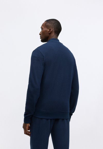 Temno modra sweatshirt iz teksturirane tkanine, s rebrastim ovratnikom in manšetami, nekoliko sproščenega kroja in preprostim dizajnom.