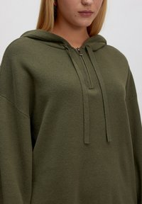 Olijfgroen oversized hoodie van textuurmateriaal, met een half-rits hals, capuchon en trekkoorden voor aanpassing.